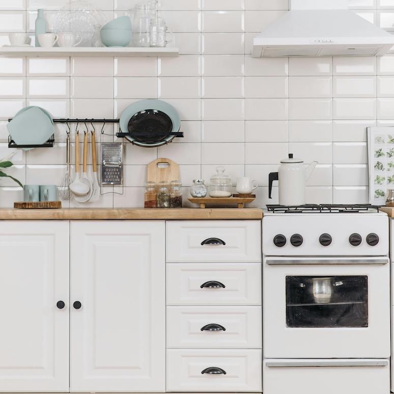 White Wooden Kitchen Cabinet With Kitchen tools hanging from wall rail against a white subway time backsplash