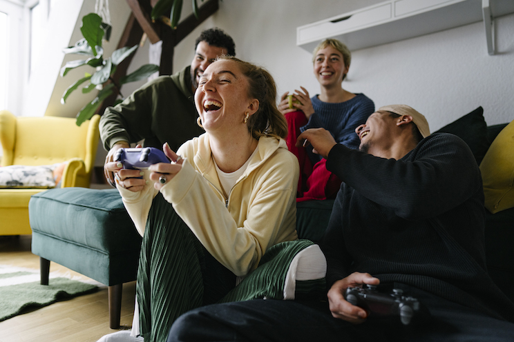 View from below of a group of Generation Z friends sitting together playing on the console and laughing out loud