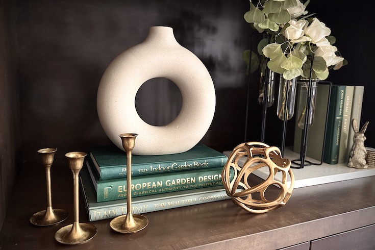 Gold accent accessories placed in front of books and a hollow circular vase.