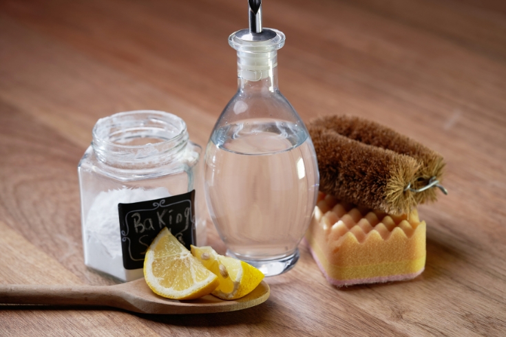 white vinegar baking soda and lemon on wooden tabletop.