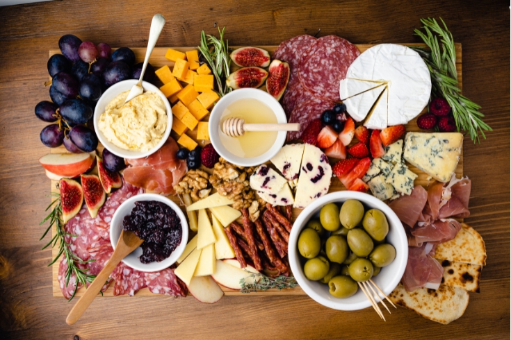Grazing/charcuterie board with cured meats, cheeses, olives, fruits and honey.