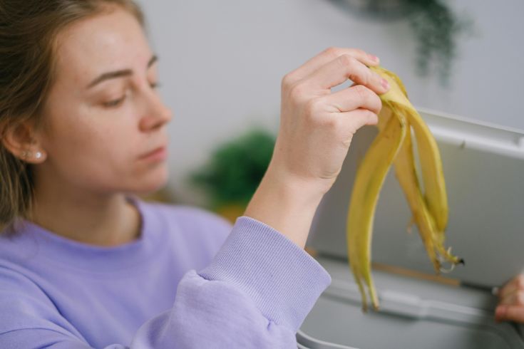 A person holding a banana peel over a bin.