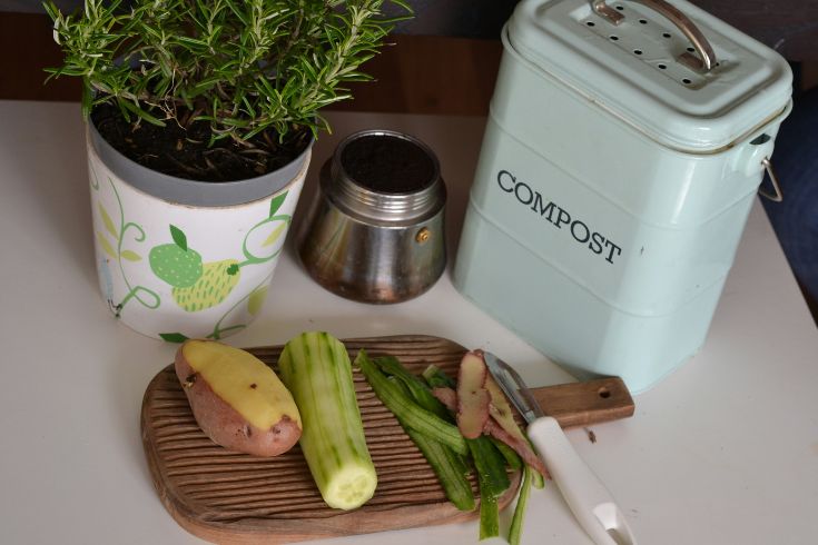An overhead shot of vegetables and herbs being prepped beside a compost bin. 