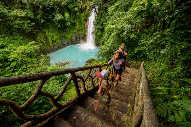 A family hiking at Rio Celeste waterfall in Costa Rica surrounded by lush forest greenery.