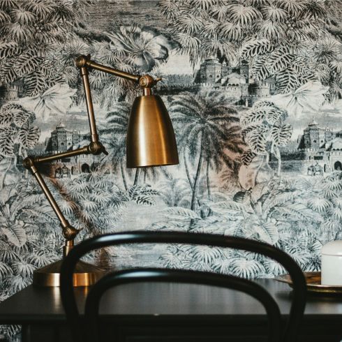 Black and white decorative wallpaper featured above a table and a brass lamp.