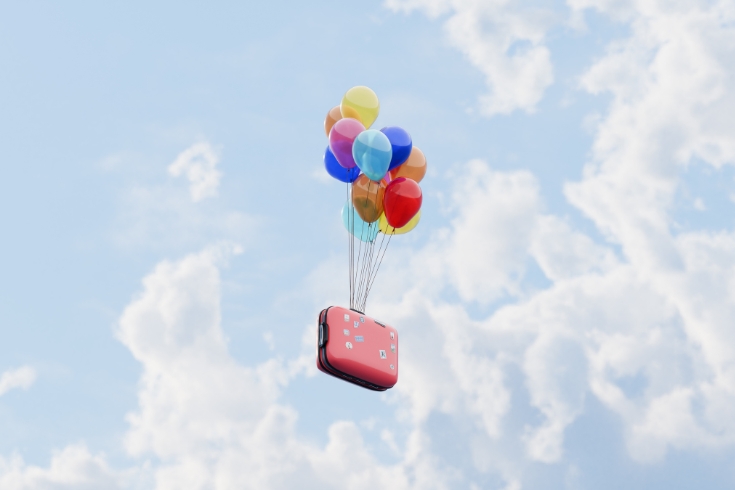 A red suitcase being lifted by balloons and flying away on a journey.