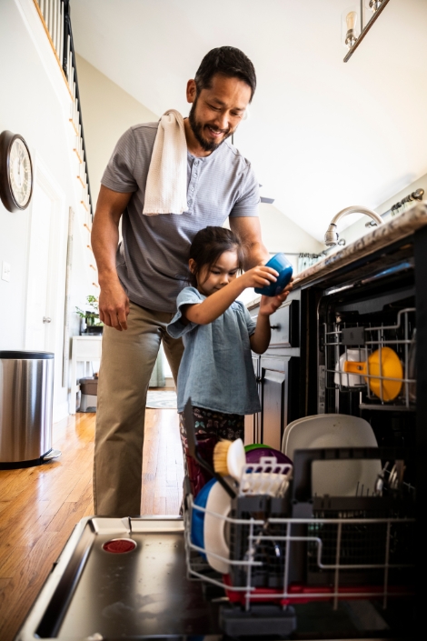 Father showing young daughter how to load dishwasher.