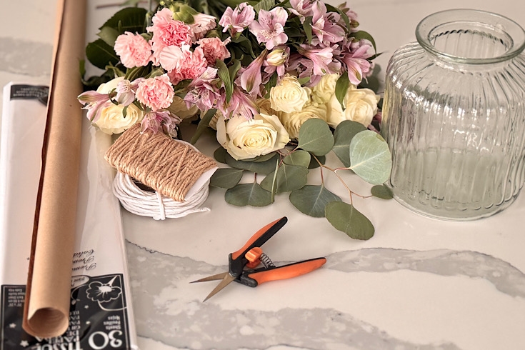 Flowers and greenery laid out on the table with tools and a glass vase.