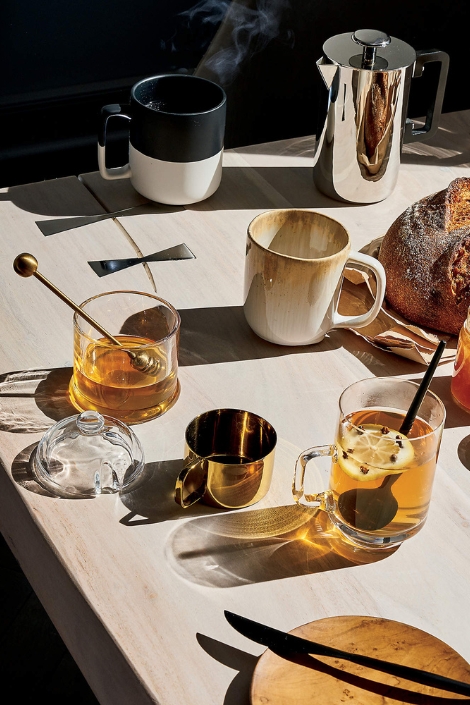 CB2 Swarm Glass Honey Pot and Dipper featured with mugs and snacks on a table.