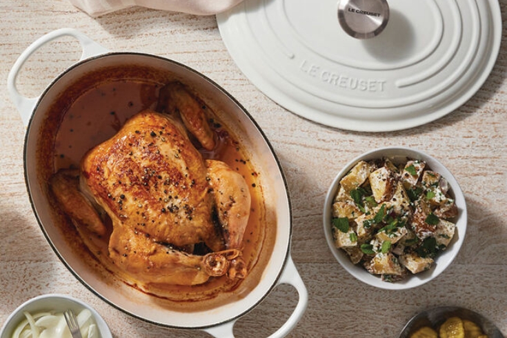 A roasted whole chicken in a white Le Creuset Oval Dutch Oven and a salad.