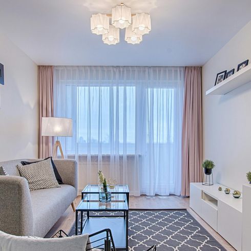 A bright living room with sheer white and pink drapes in a large window.