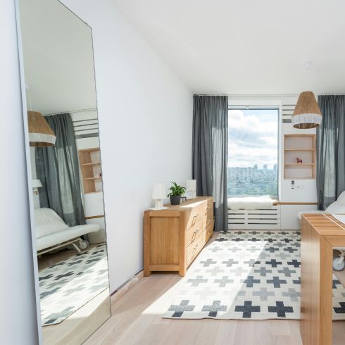 A bright light bedroom with a large full-length mirror leaning against a wall.