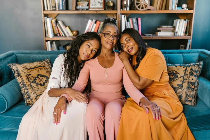 Mother and daughters lean on each other on a blue couch as part of HOME Network's post on Gen Z Home Co-Ownership with their parents 