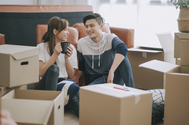couple sitting on floor resting after opening carton cardboard boxes in living room moving house