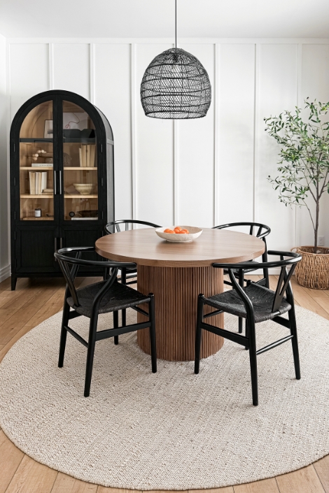 Wooden dining table with chairs against white walls wiht a black curved built'in cabinet.