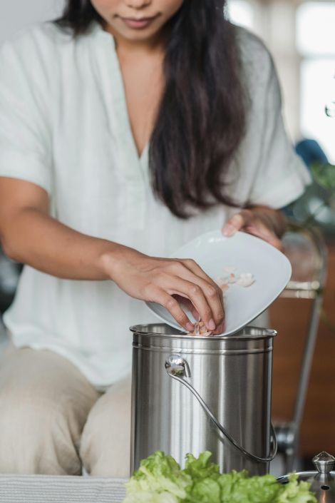 A person places food scraps from a palte into a compost bin.