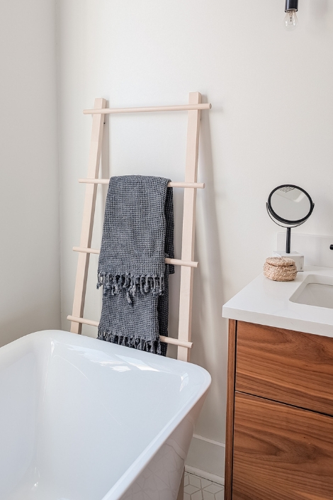 A towel ladder with a grey towel hanging behind a bathtub.