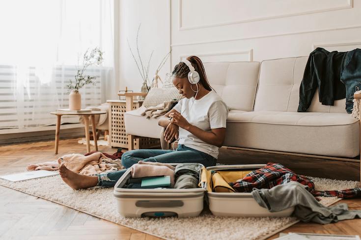 A Woman Packing a Suitcase while sitting on the floor listening to headphones