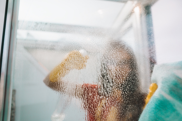 Woman cleaning and wiping window with spray bottle and rag.
