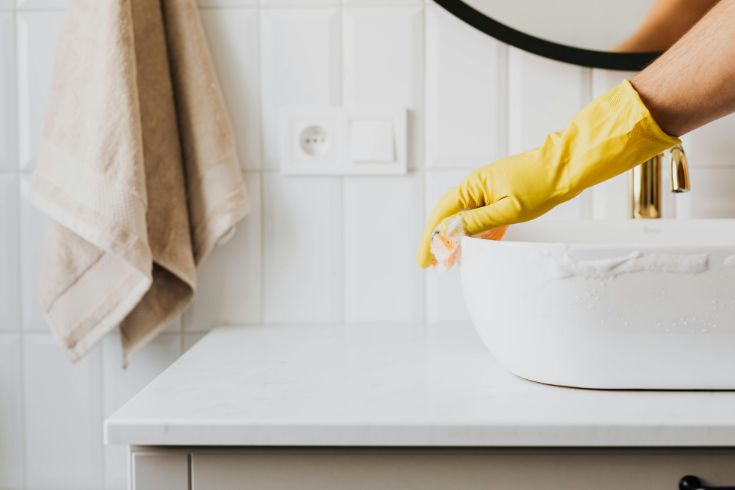 A person washing the sink in the bathroom.