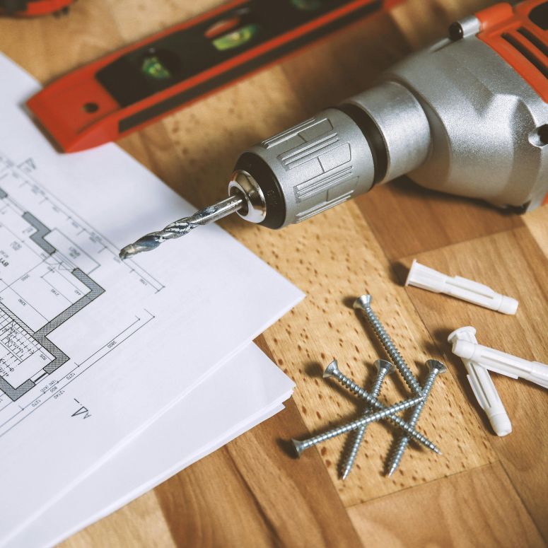 An overlay shot of a contractor's ruler, drill, screws and floor plans.
