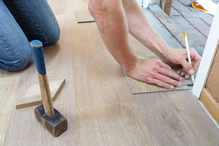 A person with a pencil points to work on an unfinished home floor. 