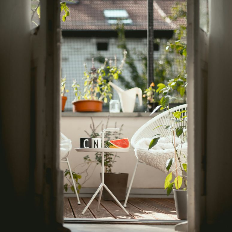 An outdoor patio in an apartment with white metal furniture and plants.