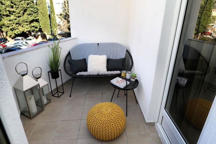 An outdoor apartment patio with a small black wicker couch and a yellow ottoman. 