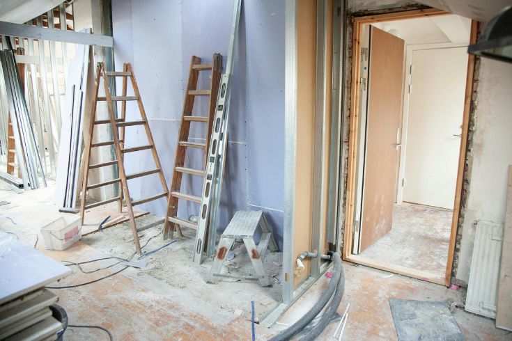 A home currently in renovation with bare floors, ladders against walls and plastic covers. 