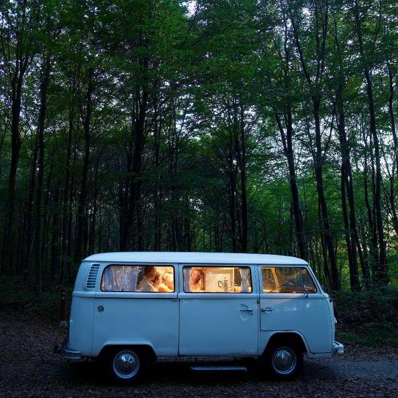 Family in illuminated van in forest, side view, evening.
