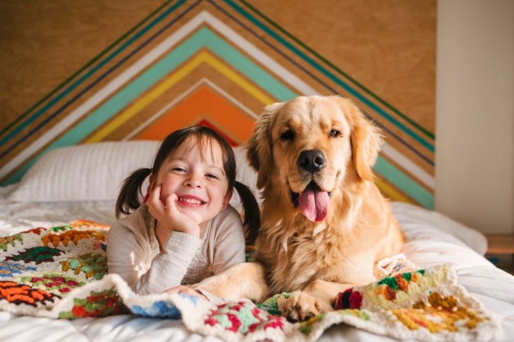 Girl lying on a bed with her golden retriever dog