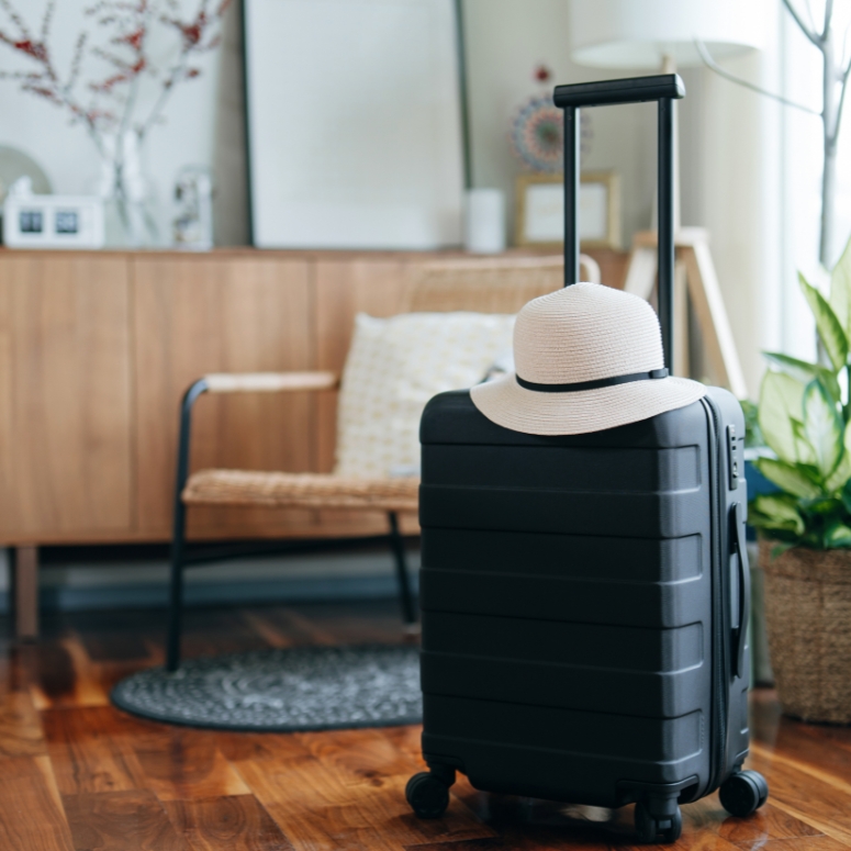 Still life of a black suitcase with a straw hat in the living room of an apartment.