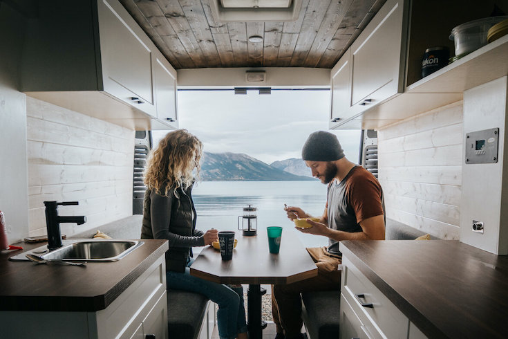 A couple eating and drinking inside a RAM Promaster RV rental from Overland Yukon