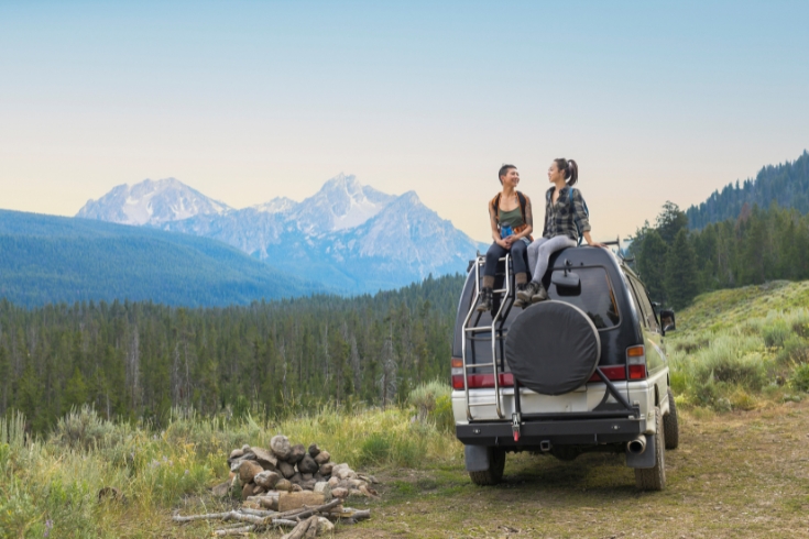 Two young woman on top of camper van in remote mountain landscape.