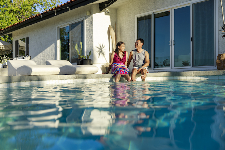 Happy couple spending leisure time while sitting near swimming pool during vacation