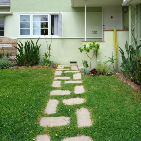 Green grass lawn with stone pathway in front of white concrete house.