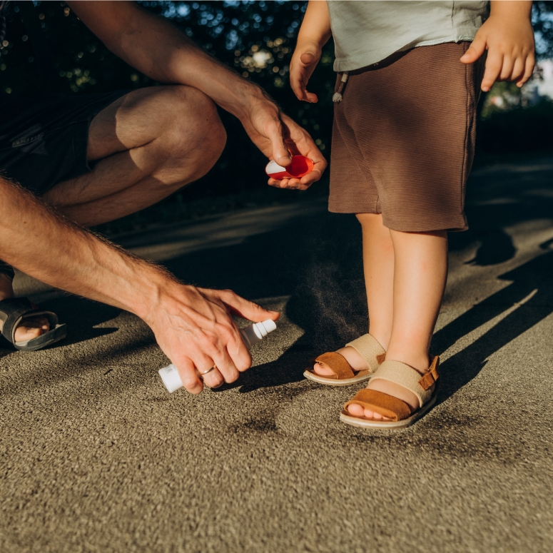 father applies mosquito spray to his son
