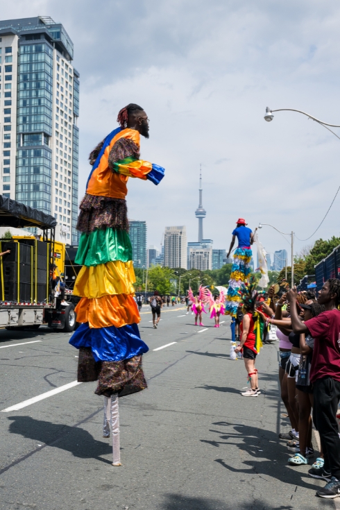 Toronto 2023 Caribbean Carnival or Caribana: Man on stilts in parade, CN tower in background.