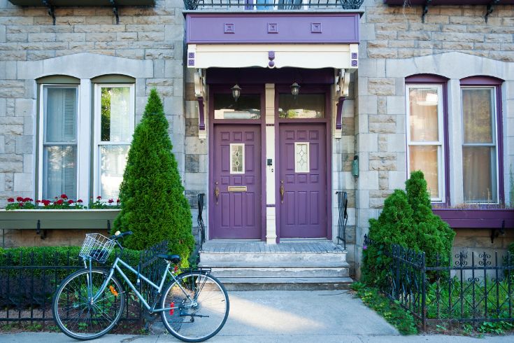 An old style house in the Plateau Mount Royal area in downtown Montreal with purple doors and trim and a bicycle parked in the front on the sidewalk.