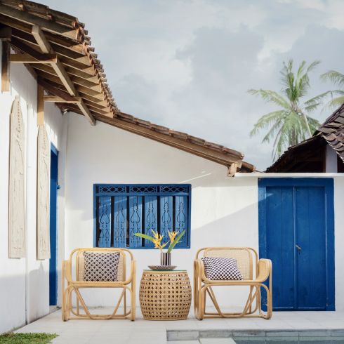 A wicker table and two chairs in front of a door painted blue.