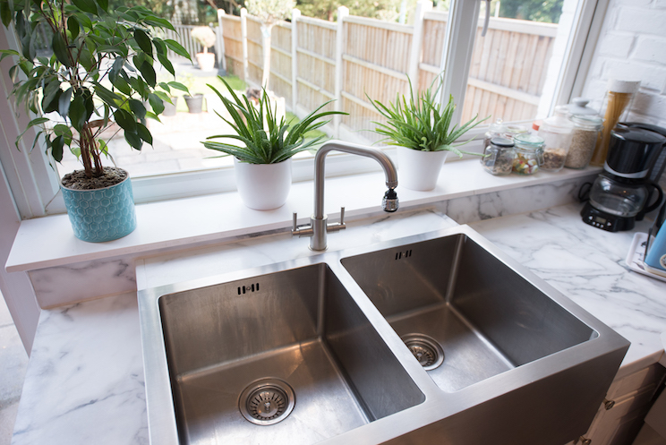 A general view of a kitchen interior with a modern stainless steel twin sinks by a window with a view into the garden