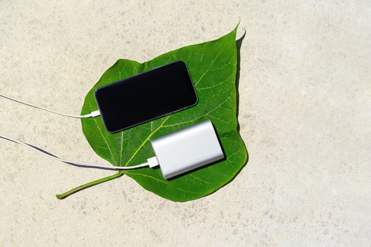 Mobile smart phone charging wirelessly by sharing battery via device on a sunny day on a background of green leaf. 