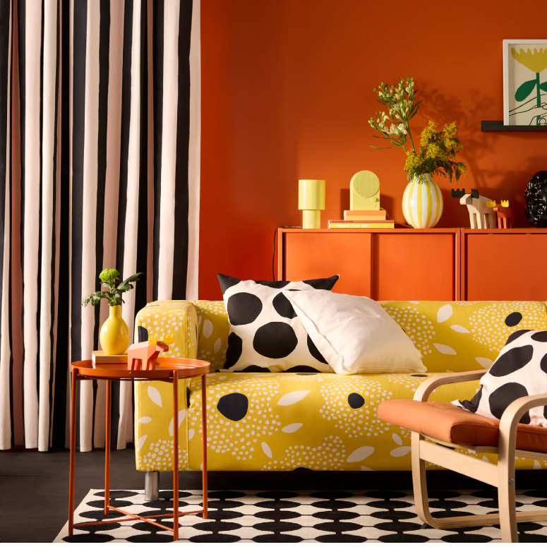 A room with various patterns: a dotted carpet, polka dot pillow, striped curtain and patterned couch
