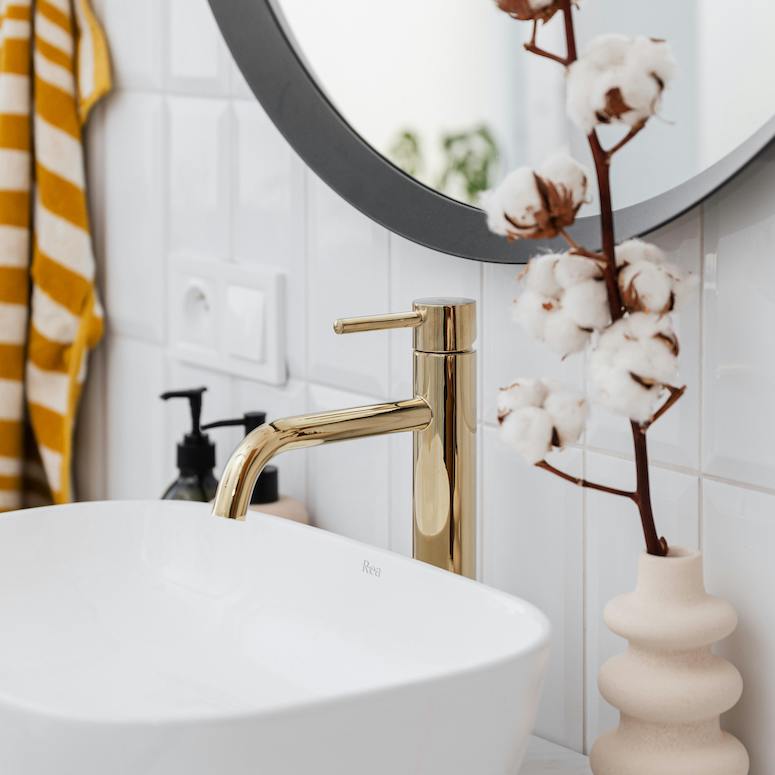 Gold Faucet and a white sink Below a Mirror in a white tile bathroom