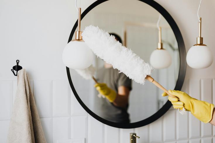 Woman dusting lamp in a bathroom for a HOME Network post about bathroom cleaning