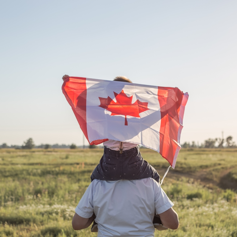 Man and boy on his shoulder holding Canadian Flag.