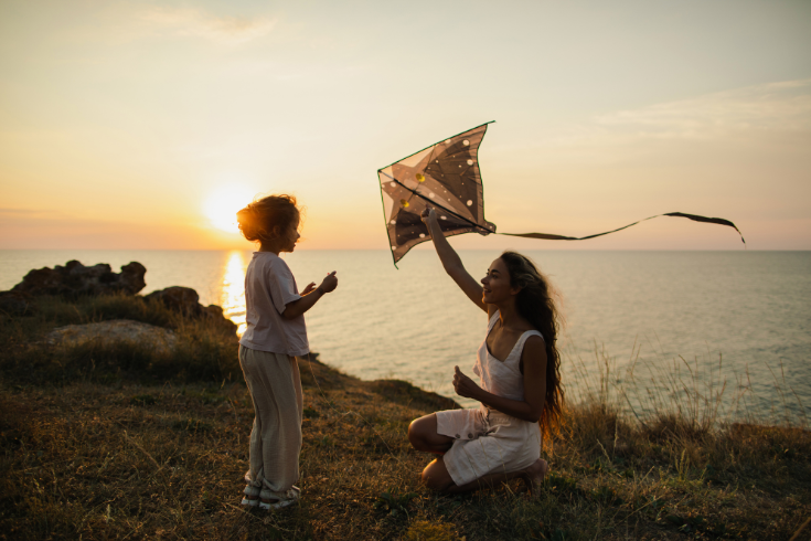 Mom playing together with daughter outdoors with sunset coastline scenery. 