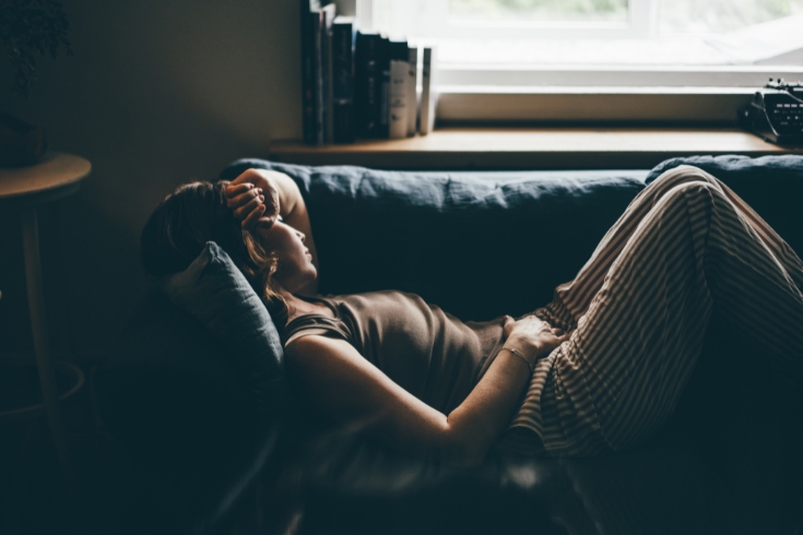 Depressed woman lying on sofa at home.