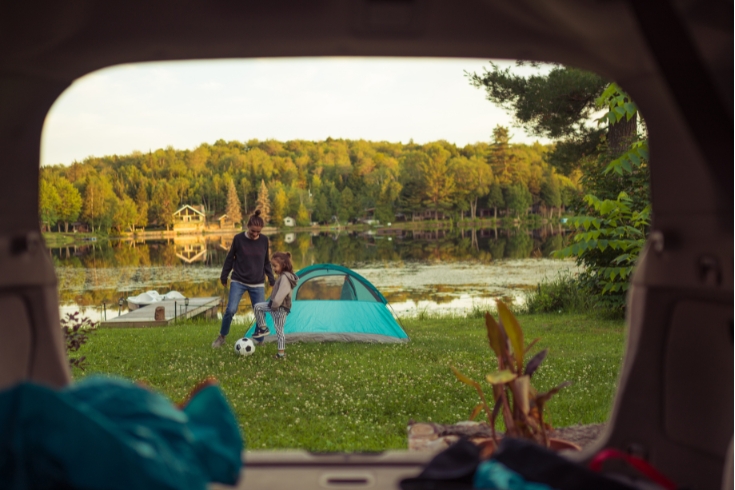 Mother and daughter playing soccer by the lake.View from the car. The camping tent is setup ready for the night.