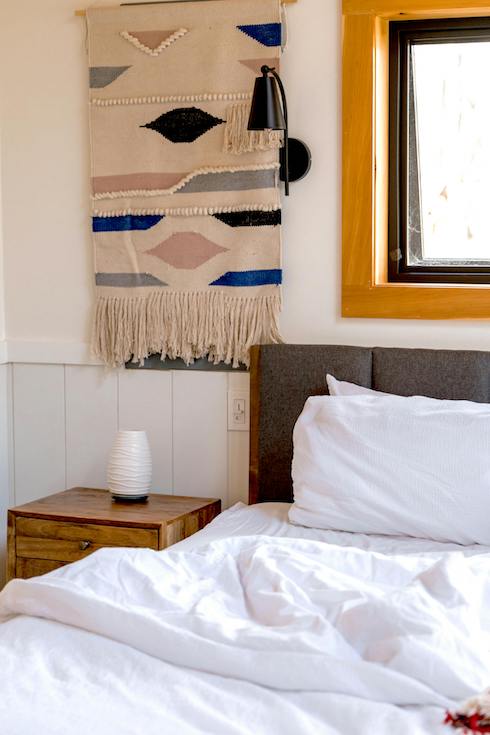 A White Ceramic Pot on Wooden Side Table Beside Bed with a tapestry on the wall beside a bed in a comfy bedroom